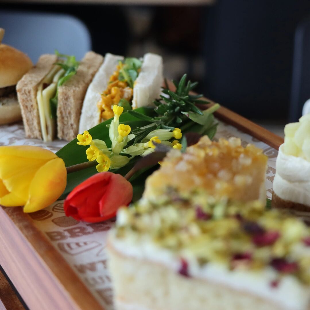 An afternoon tea platter featuring freshly made sandwiches, sliders, cakes and scones with colourful tulips.