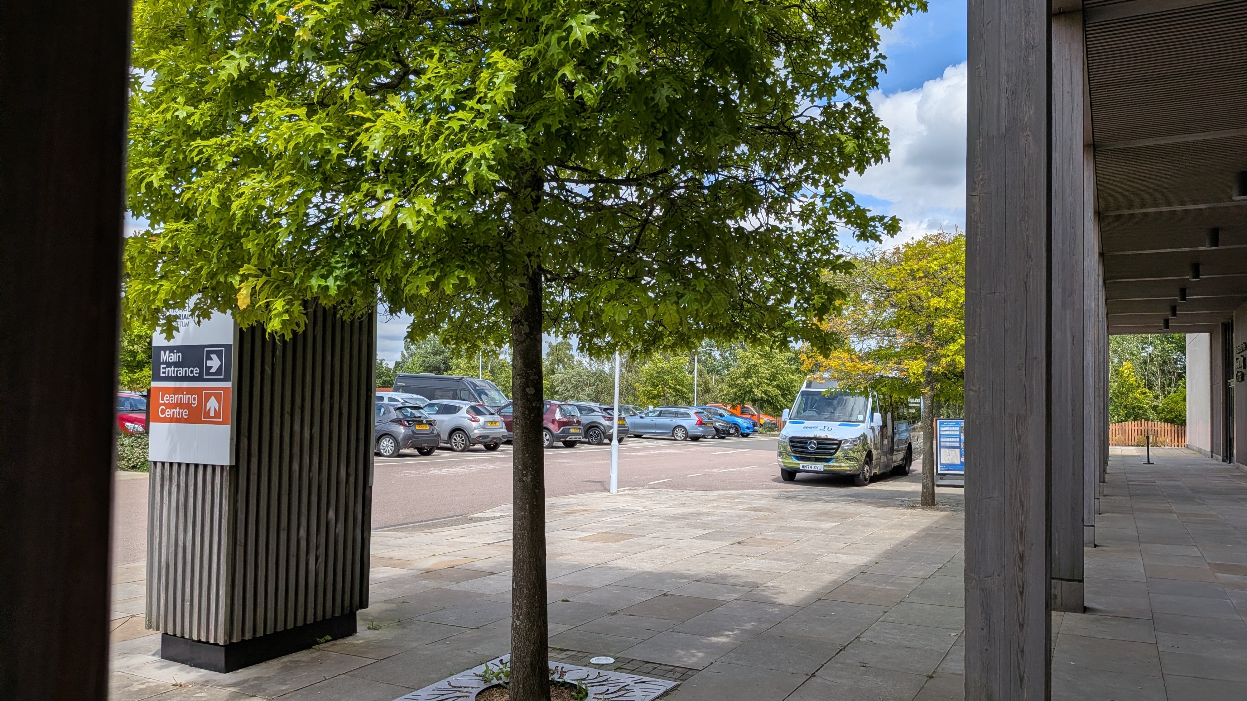 View of the Arboretum car park, featuring a row of cars and the Arboretum bus waiting to collect passengers.