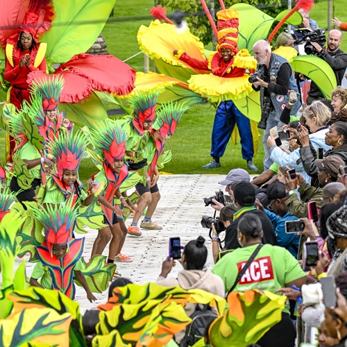 Image shows a crowd of young people in red and green carnival dress performing in front of a crowd