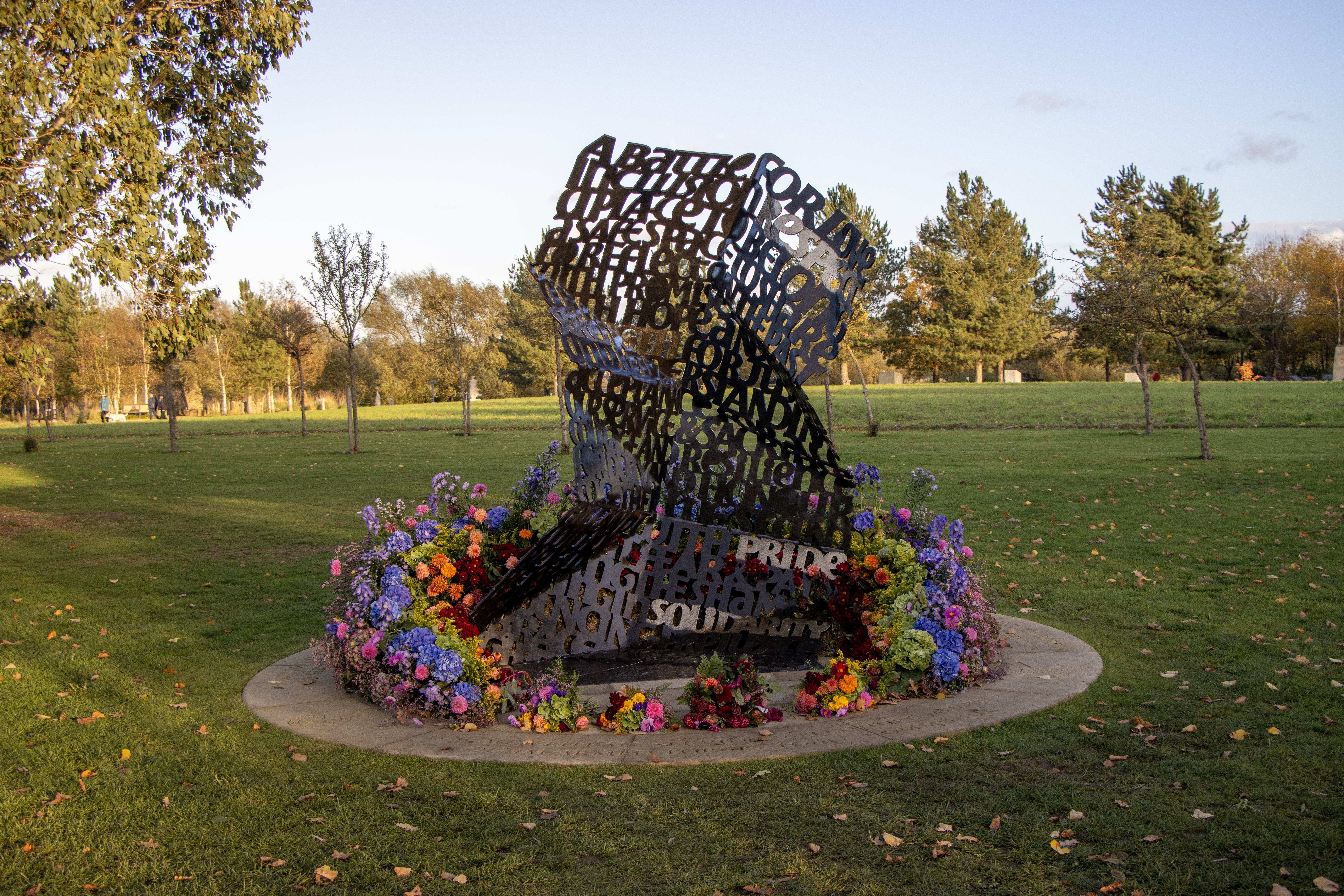 The LGBT  Armed Forces Community Memorial on dedication day, surrounded by multicoloured floral arrangements