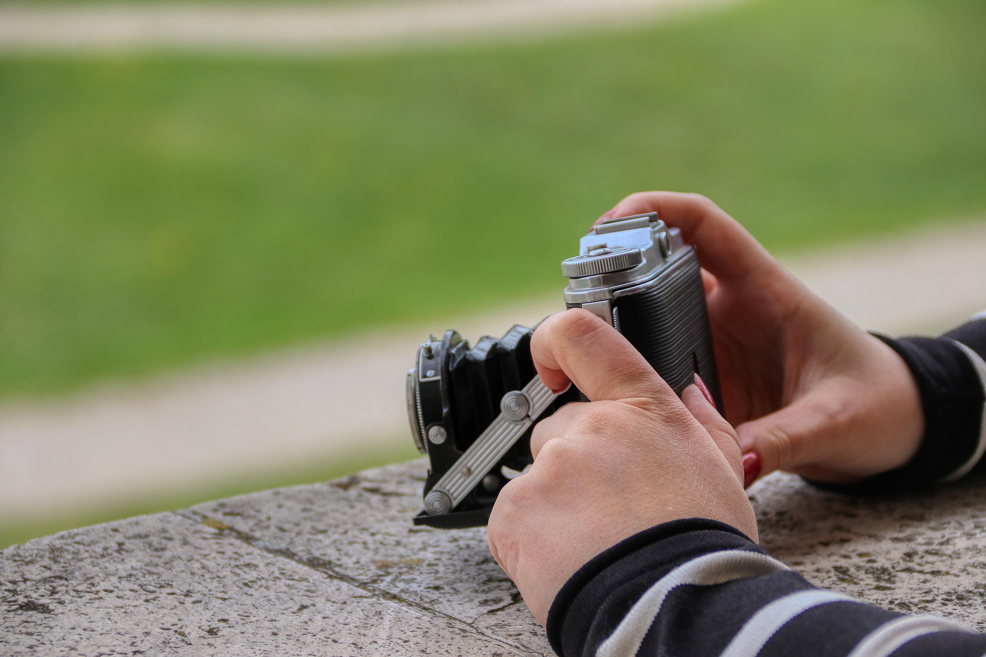 Hands grip a camera, balanced on stone with bright green grounds blurred in the background.