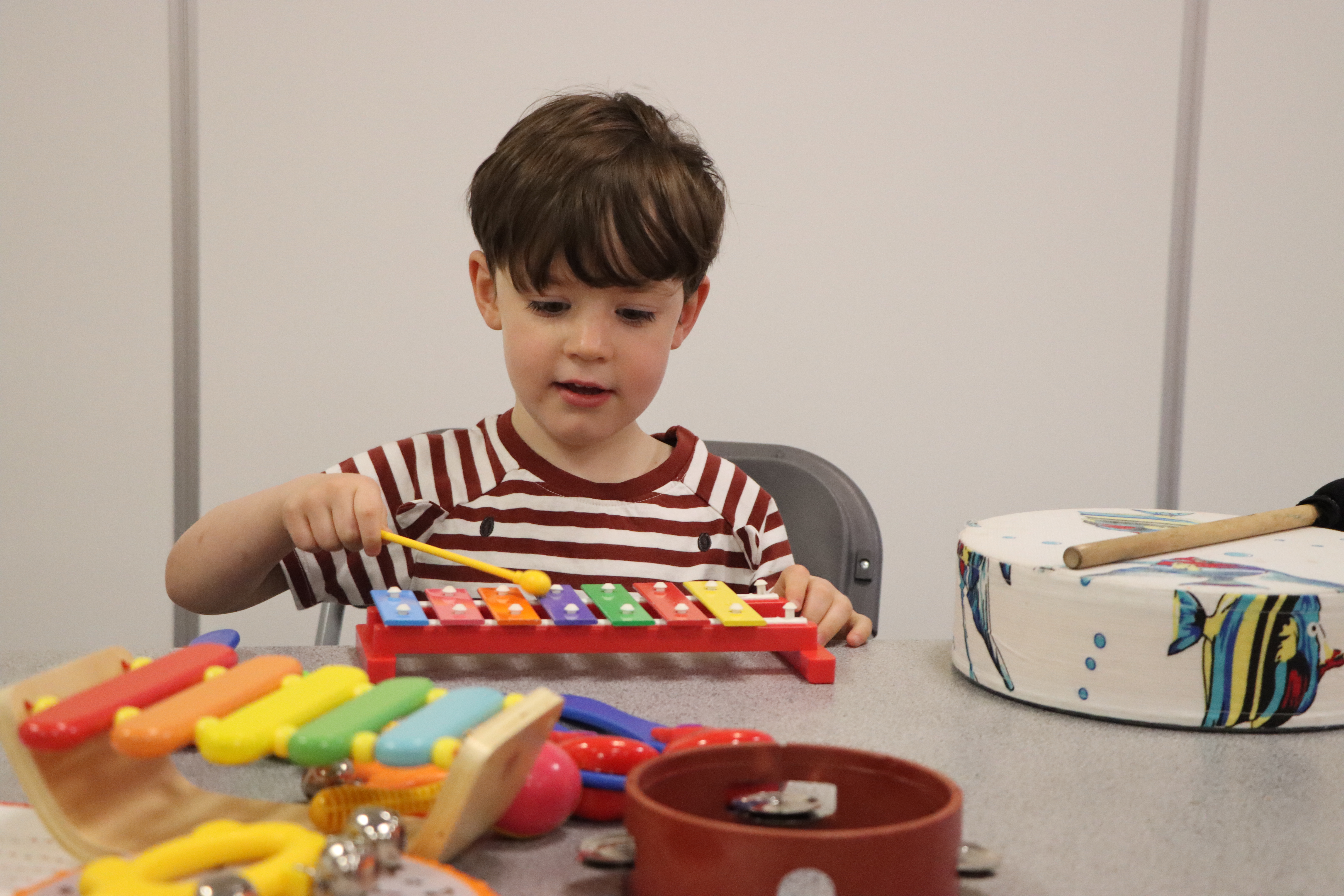A small male child making music on a xylophone as part of the music making workshop at the arboretum