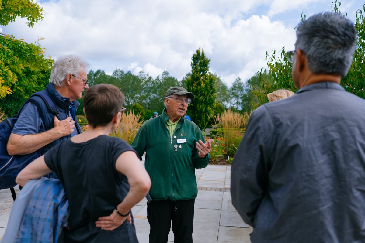A group of four adults listen to an Arboretum volunteer as he talks within Heroes' Square