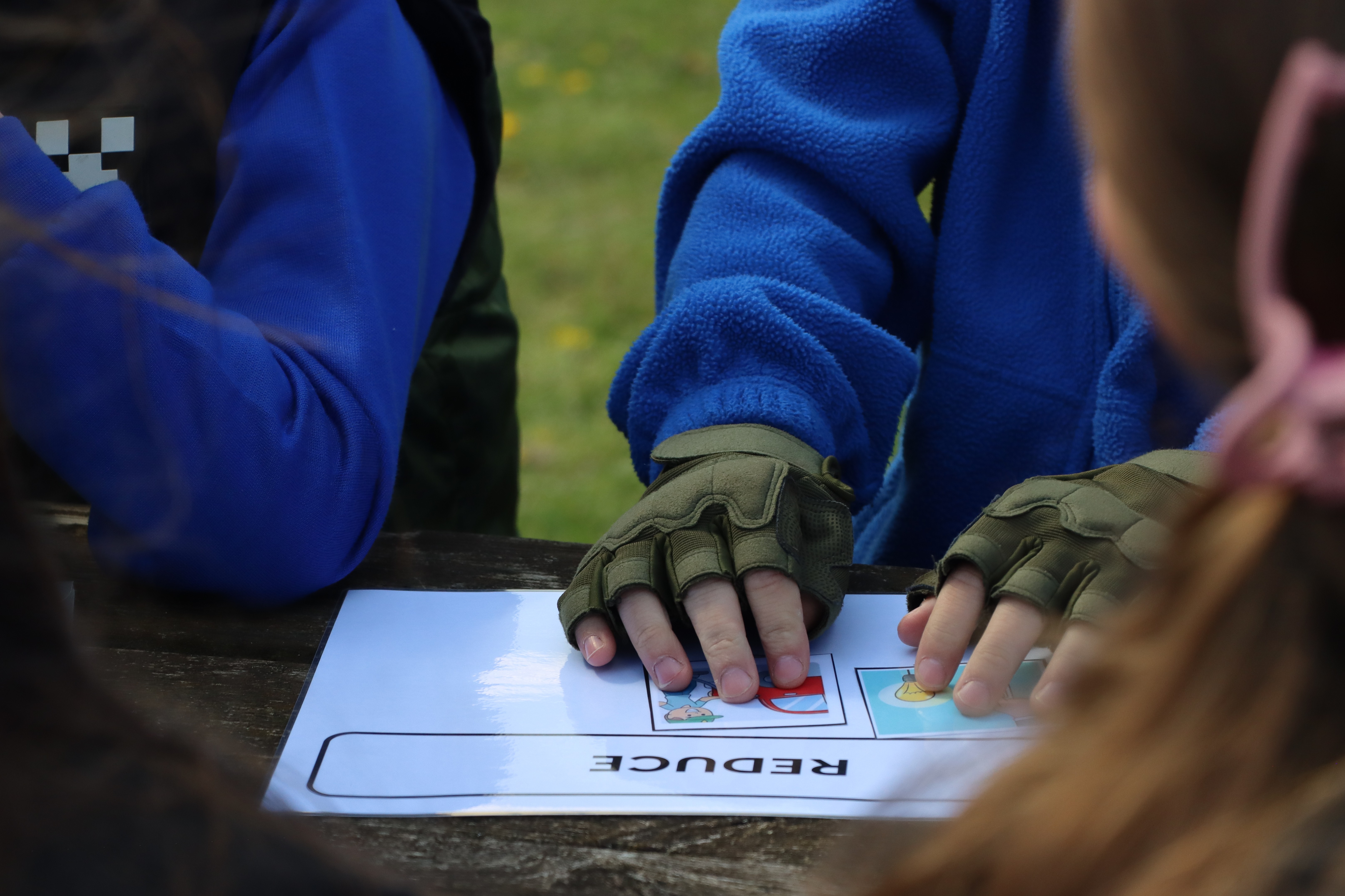 Students hands placing cards saying Reduce and Reuse on a worksheet, teaching them about waste management.