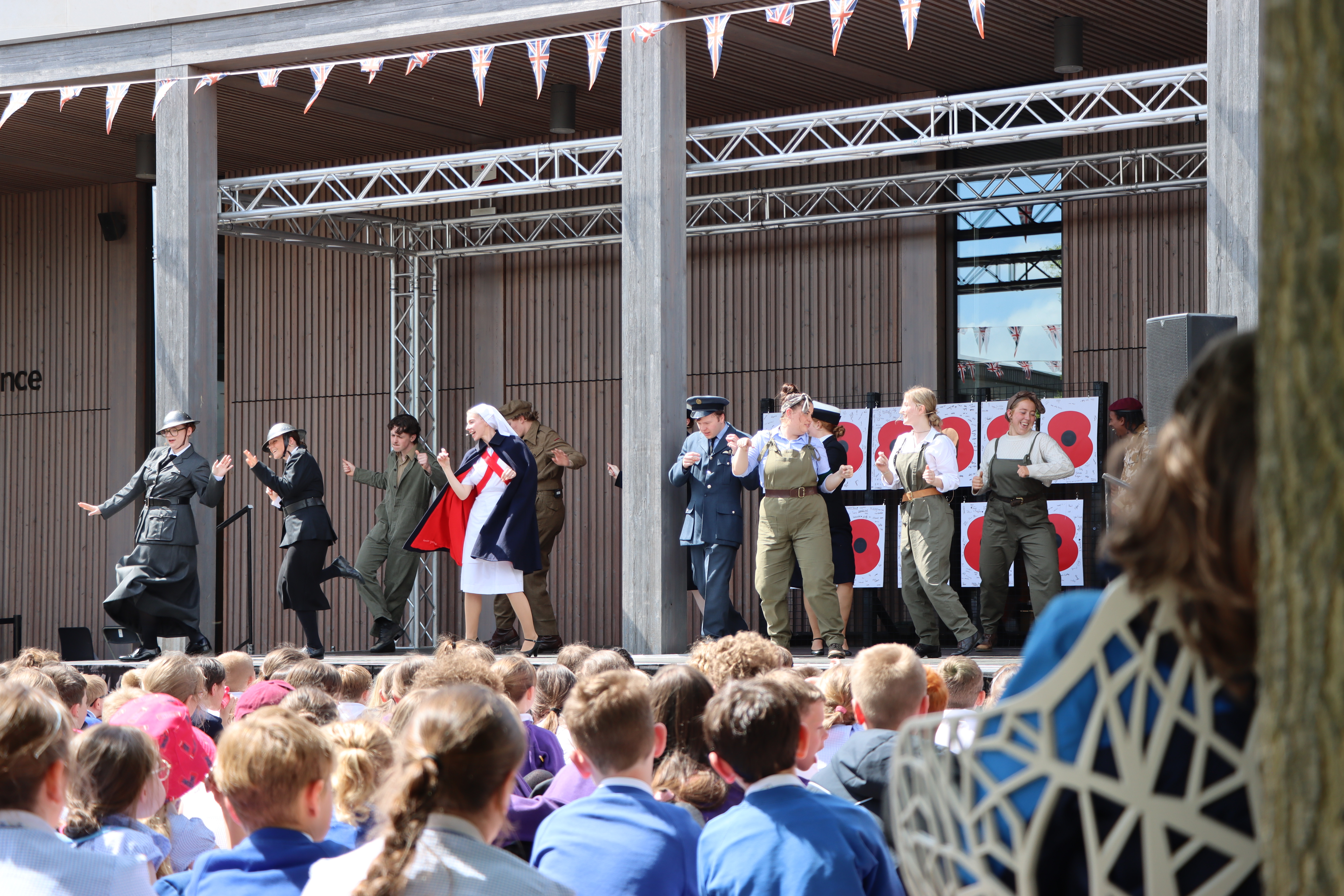 A group of World War II costumed performers perform on a stage in front of a crowd of children